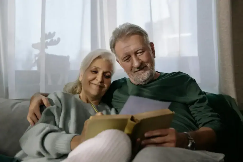 Elderly couple smiling and reading together, enjoying companionship and health at home.