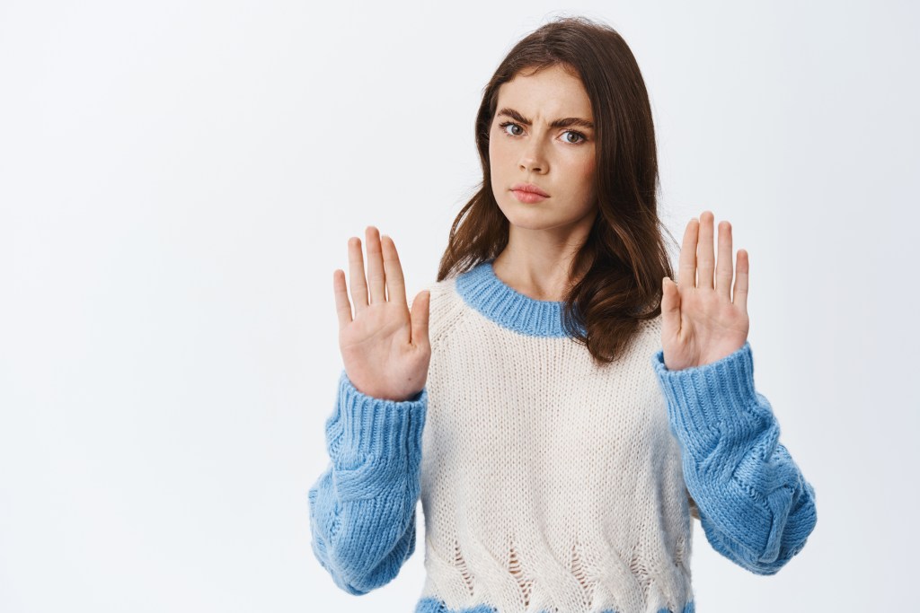 stop now serious frowning woman raising hands with block gesture saying no refusing bad offer standing sweater against white background